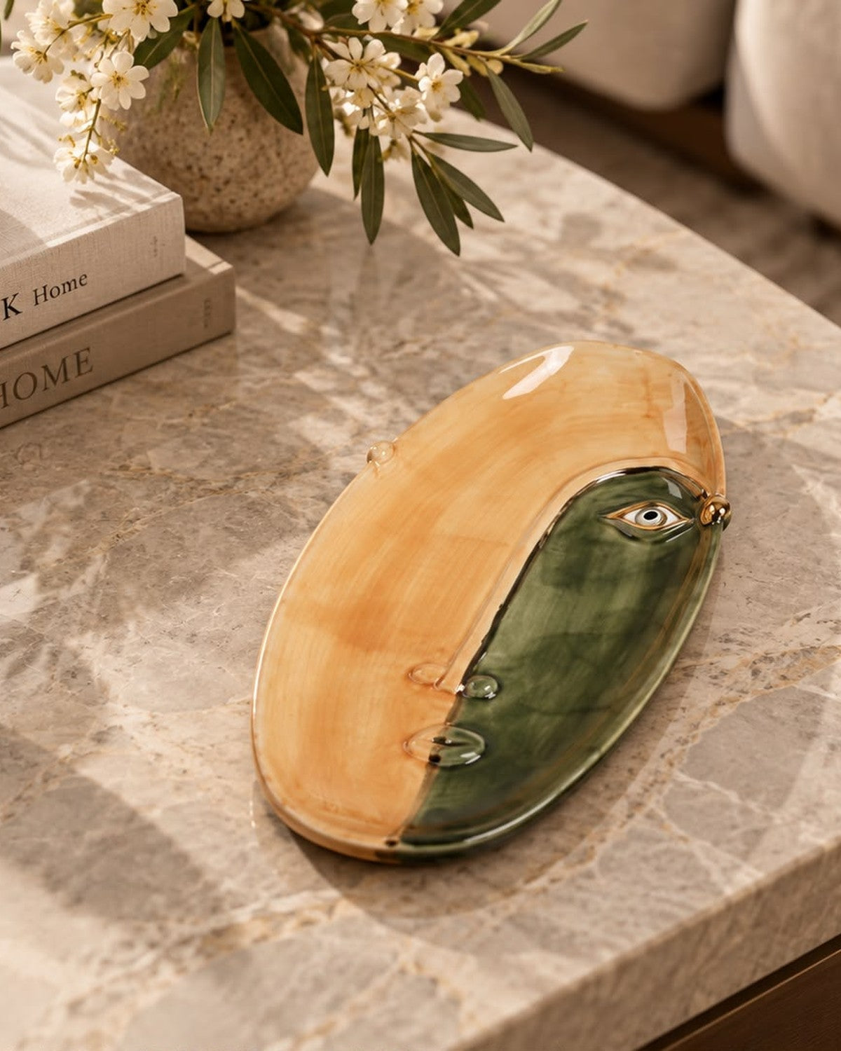 Styled on a console: An oval plate with a glossy, abstract face design in green and beige