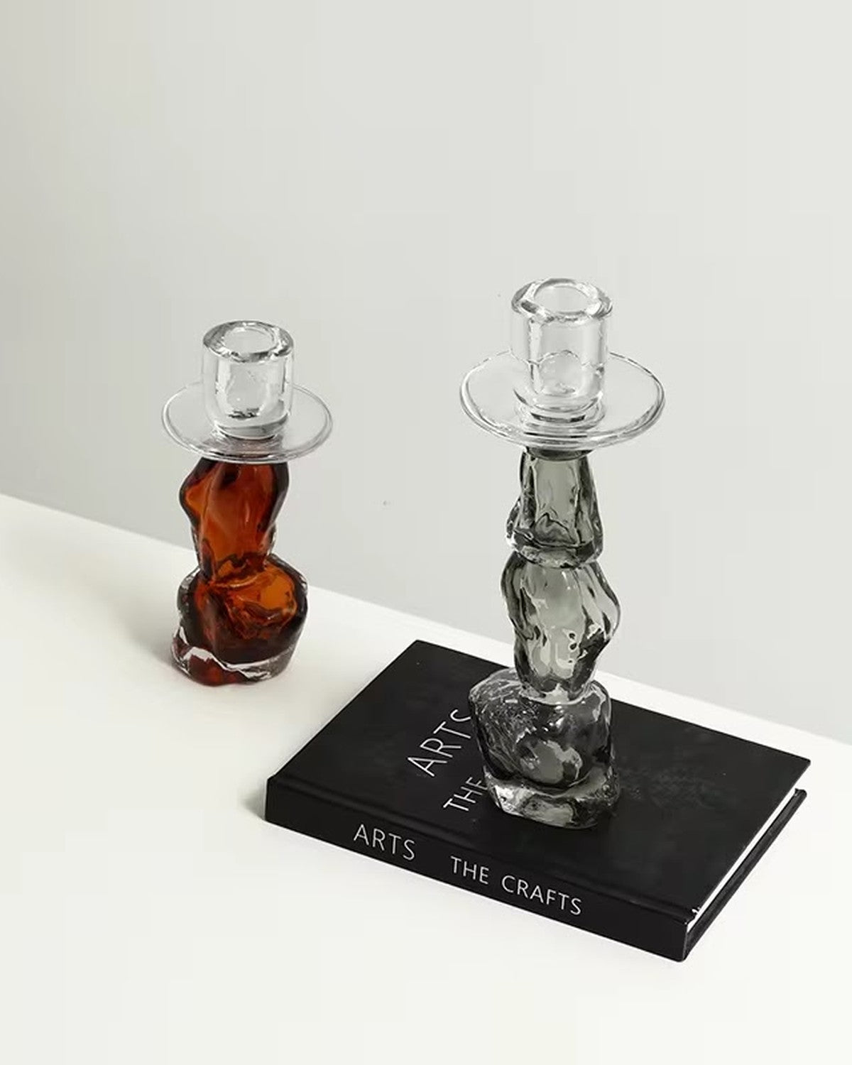 On a plain background: Amber and smoky wavy glass candle holders, one on a black book