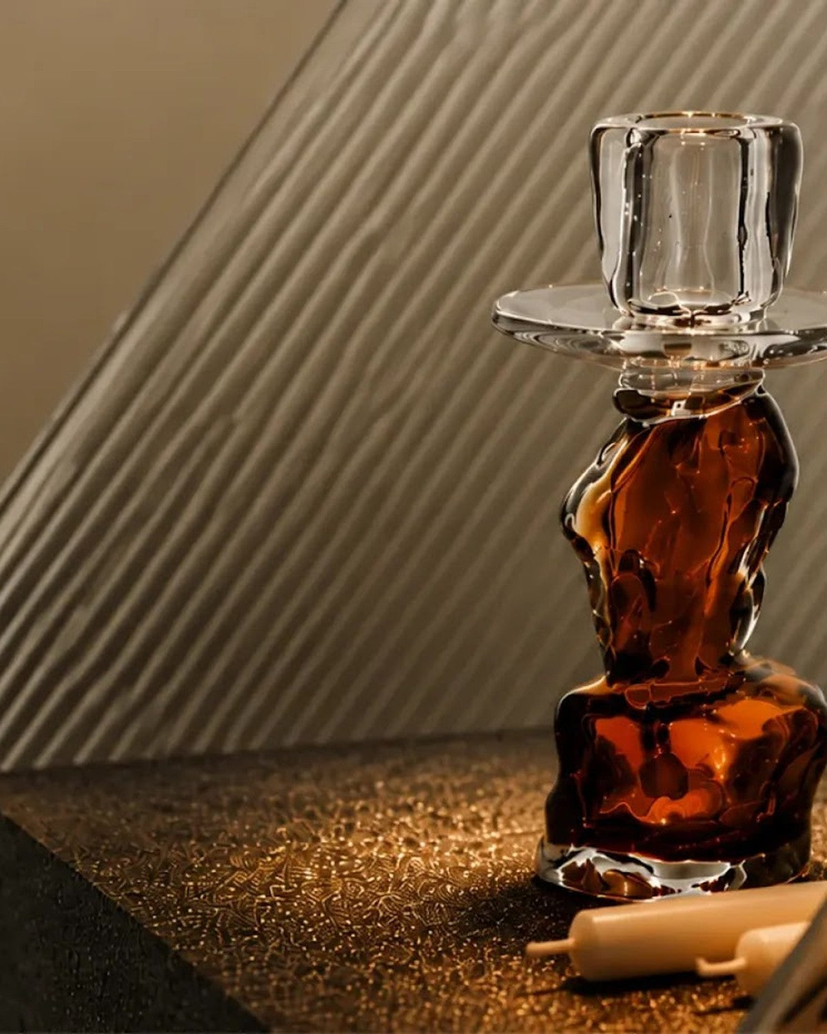 Close-up of an amber and clear candle holder on a dark patterned surface