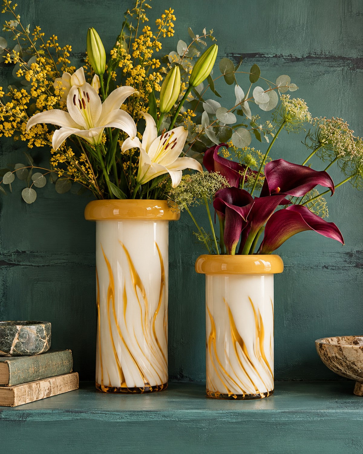 Styled on a green surface: a yellow-striped vase holds lilies and greenery
