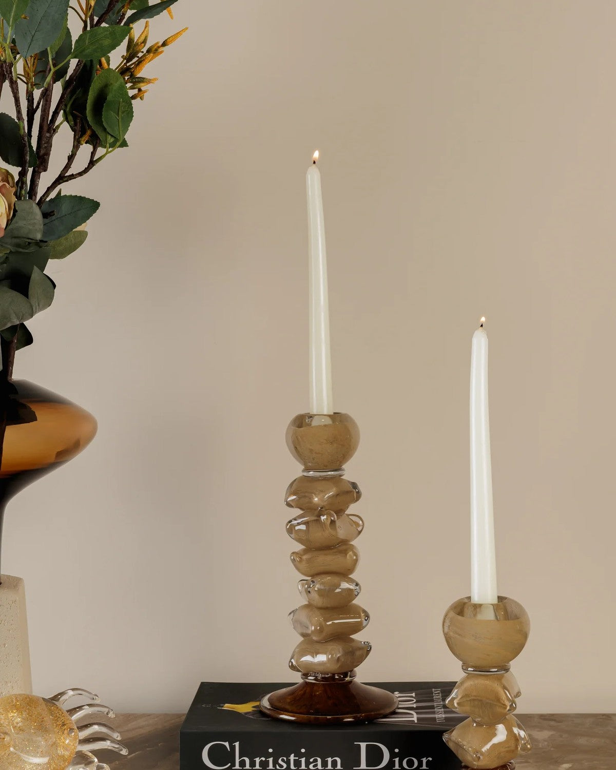 Close-up of two lit white taper candles in stacked, translucent amber holders