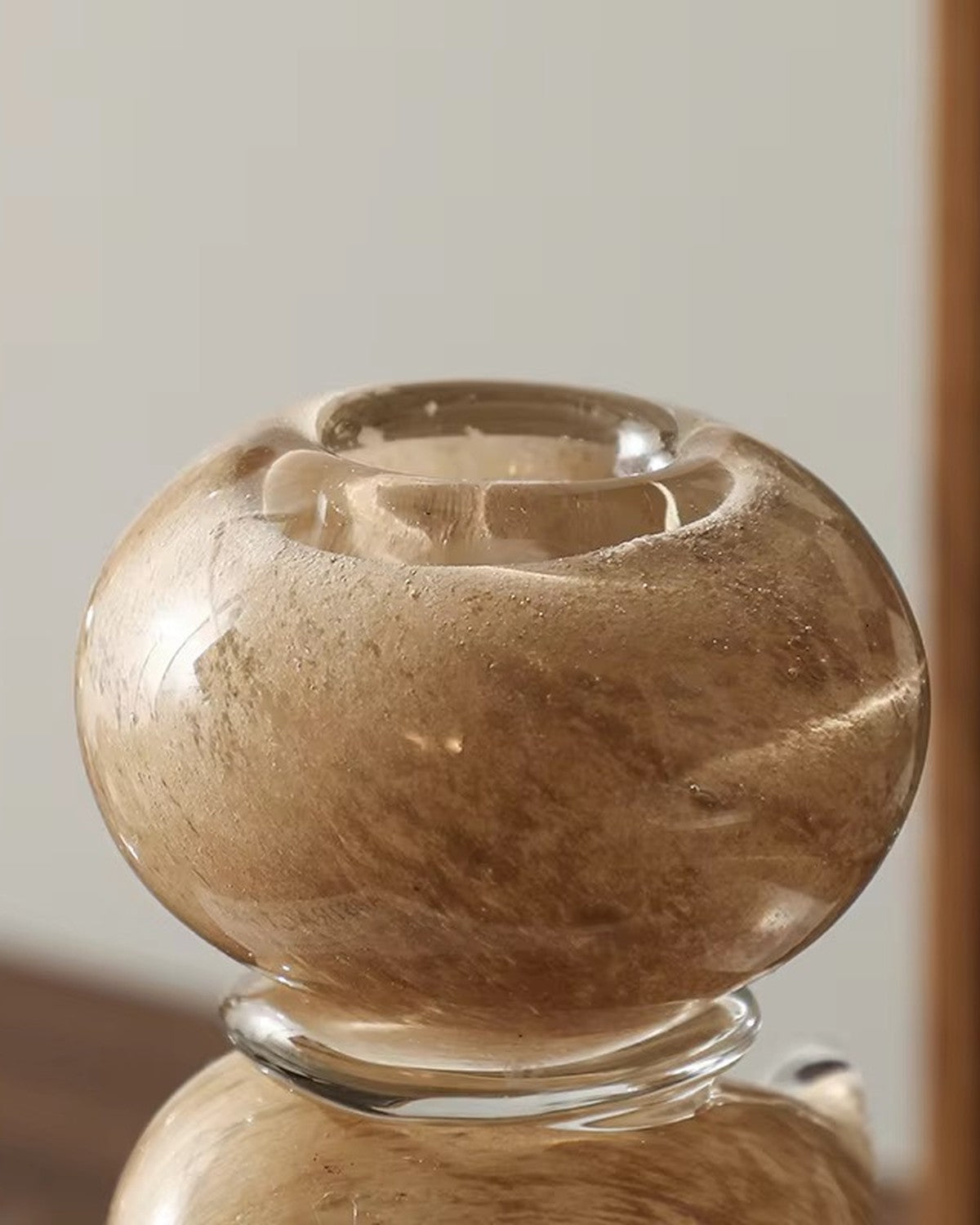 Close-up of a round, amber-brown candle holder with swirling texture, on a clear base