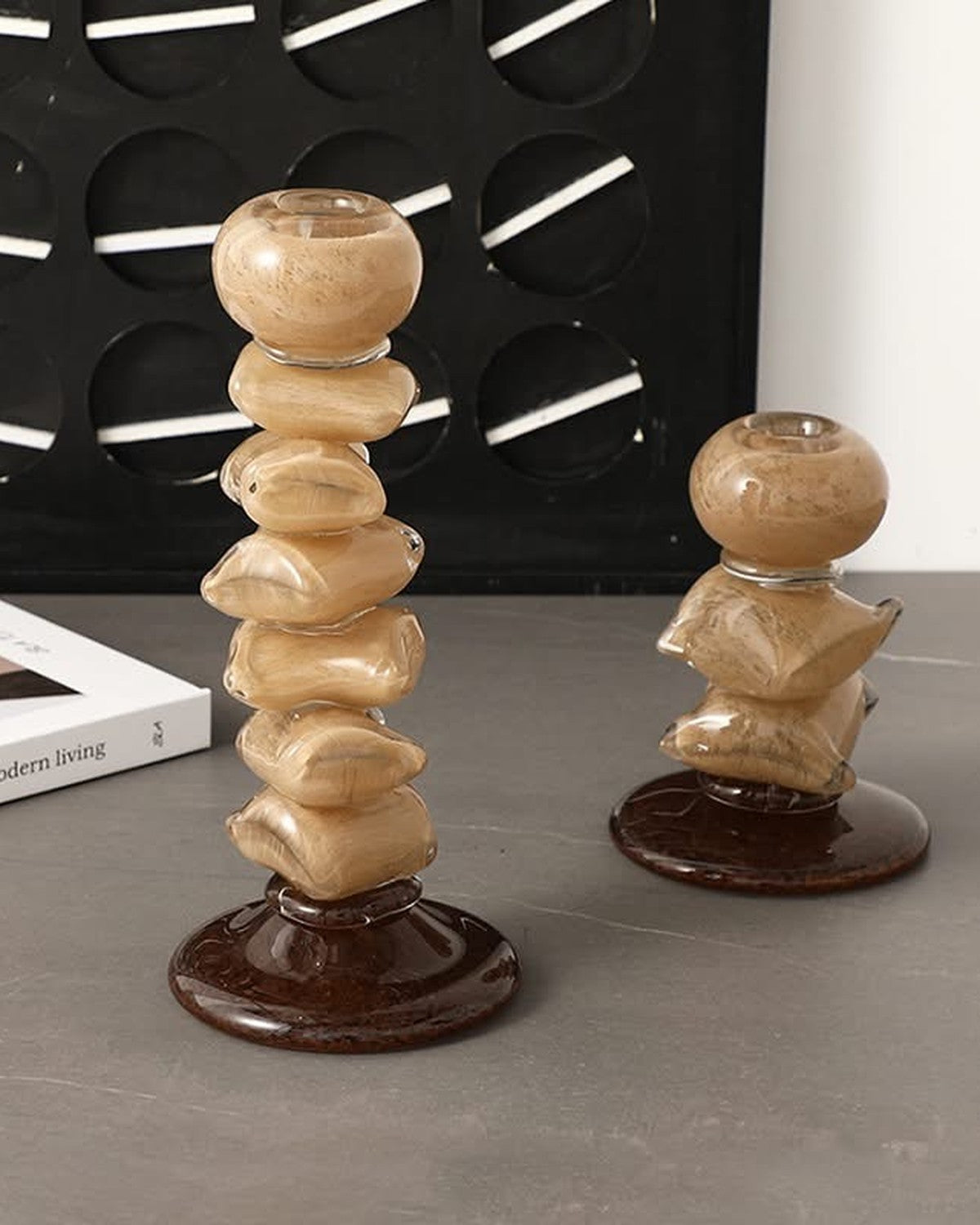 Close-up of two stacked, glossy, light brown pebble-shaped candle holders on dark bases