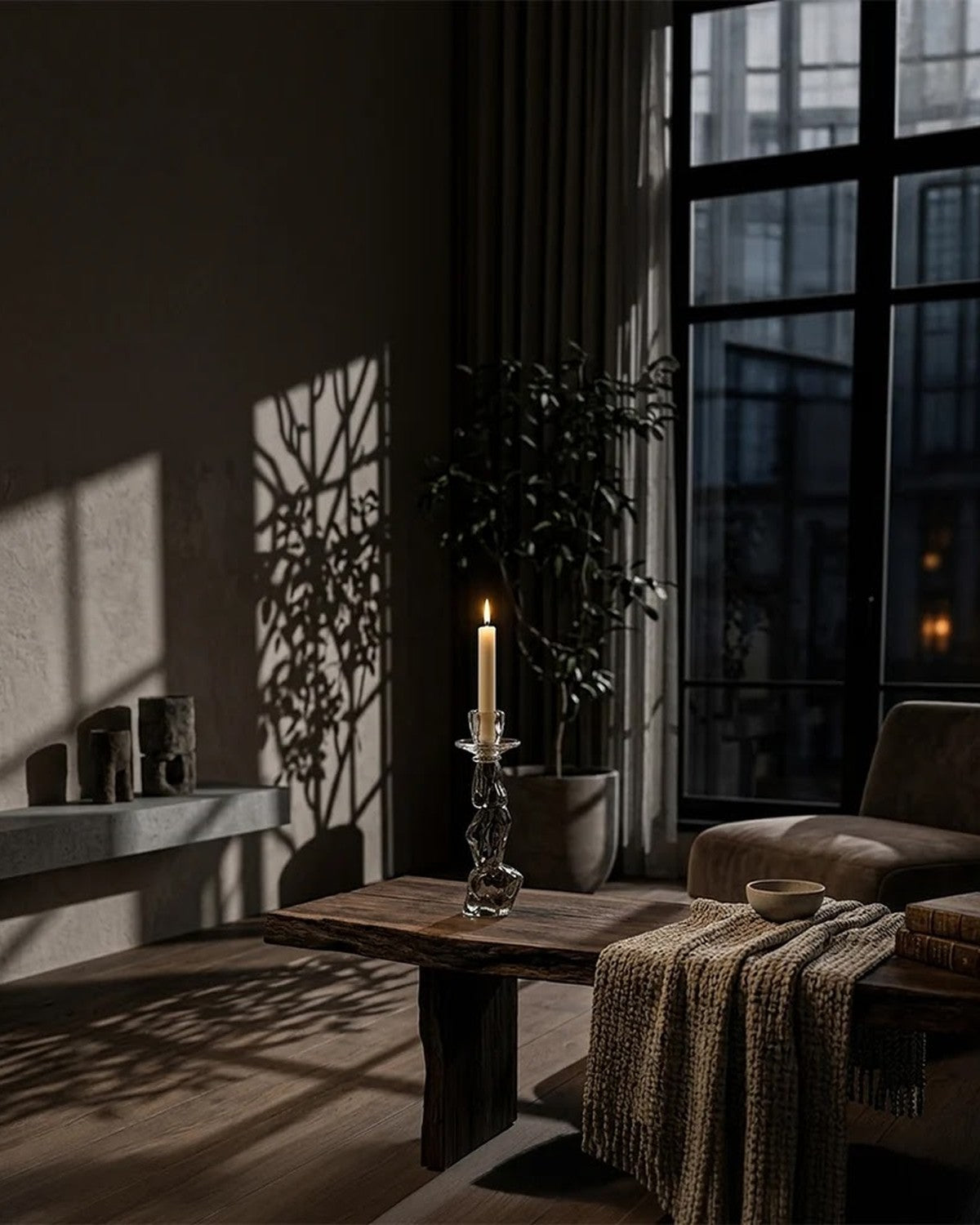 In a living room: Sculptural glass candle holder with lit candle on dark wood table