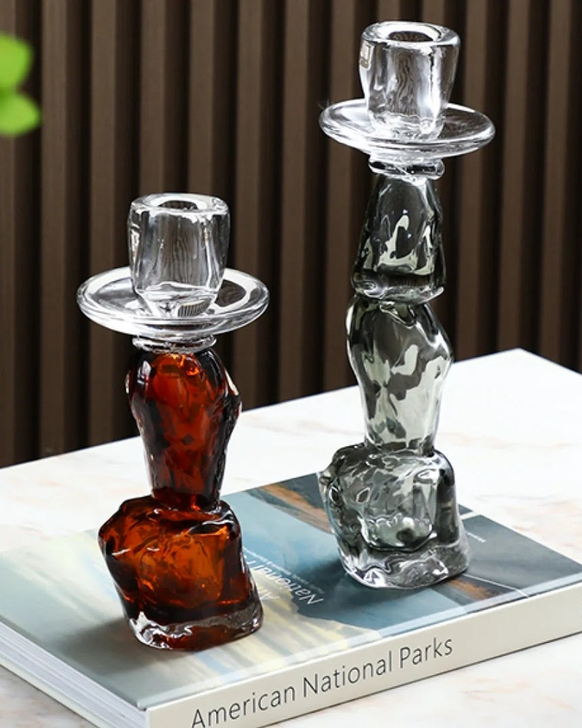 Close-up of two irregular, clear, amber and smoky candle holders on a book